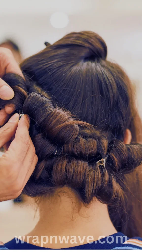 Close-up rear view of a woman's dark brown hair being styled into a twist and pin method for heatless curls. Hands are shown wrapping and securing multiple coiled, rope-like hair sections into small buns around the back of her head using small metal sectioning clips. The website watermark "wrapnwave.com" is displayed clearly at the bottom.