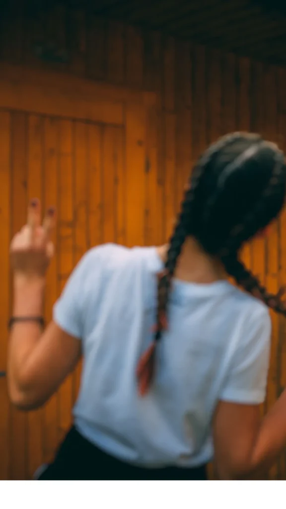 Back view of a person with dark hair styled into two tight Dutch braids, showing a heatless method to create beach waves for long hair.
