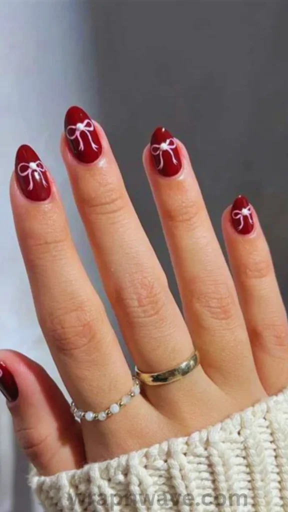 Long glossy dark red and black ombre nails adorned with black 3D bow charms. Ideal inspiration for dark coquette and moody winter nail designs.