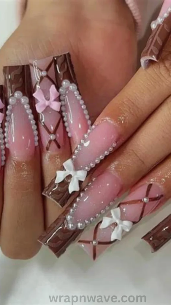 Close-up of long, square-shaped acrylic nails with pink bases, chocolate brown sweater-knit French tips, pearl outline accents, crisscross ribbon linework, and 3D sculpted white and pink bow charms. A dramatic visual example of maximalist 3D bow nail art and coquette manicure trends.