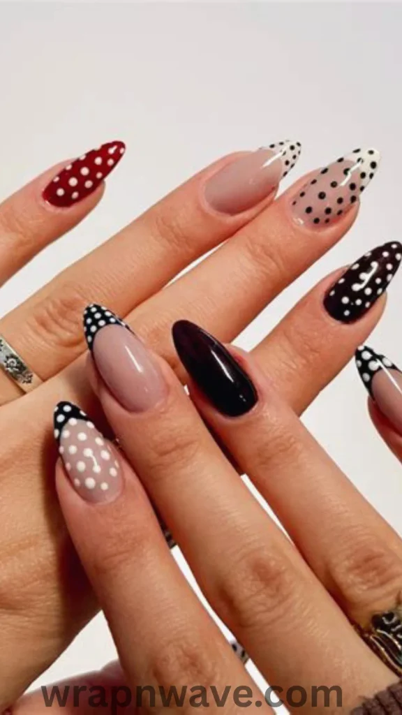 Close-up of hands with long, almond-shaped nails featuring a mix-and-match polka dot manicure in red, black, nude, and white, showcasing varied designs like dotted French tips, full-coverage patterns, and solid accent nails.